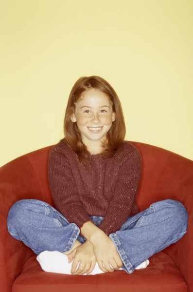 Cute young girl sitting in red chair. Photo : Fisher Litwin