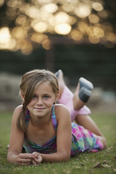Portrait of girl (8-9) lying on grass. Photo : Mike Kemp