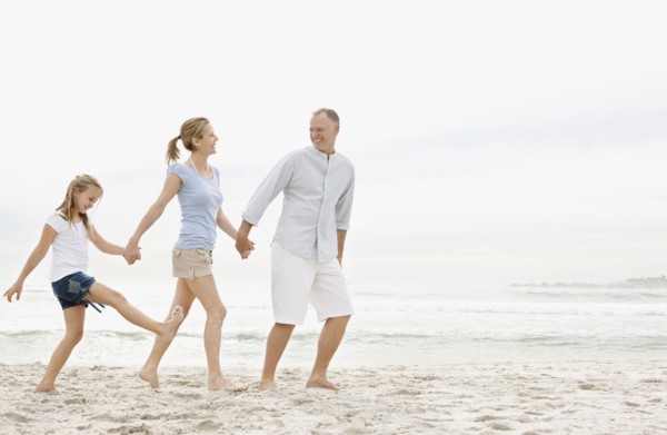 Parents with daughter (10-11) walking on beach. Photo : Momentimages