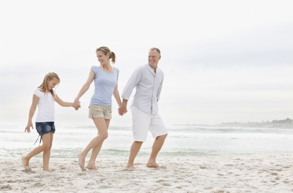 Parents with daughter (10-11) walking on beach. Photo : Momentimages