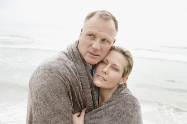Embraced couple covered by blanket looking away on beach. Photo : Momentimages