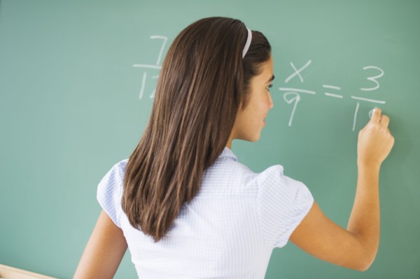 Girl (12-13) writing on chalk board in class.