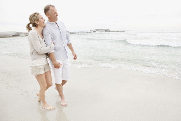 Couple holding hands and walking on empty beach. Photo : Momentimages