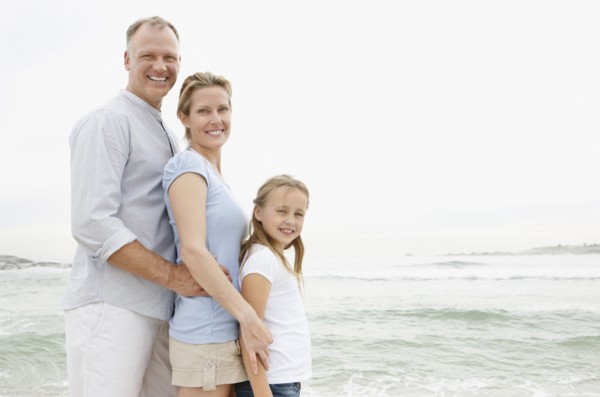 Smiling family standing at beach and looking at camera. Photo : Momentimages
