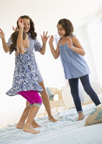 Sisters (2-3, 8-9, 12-13) jumping on bed. Photo : Daniel Grill