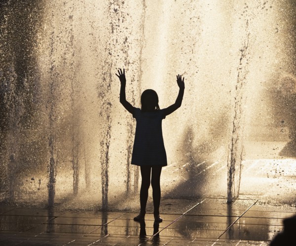 Silhouette of girl playing in fountain. Photo : fotog