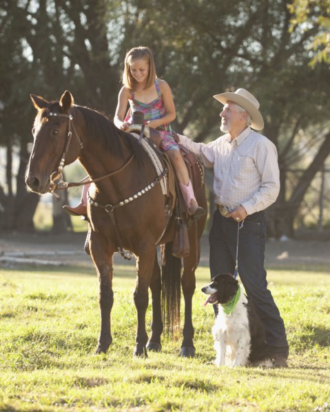 Senior man with dog assisting granddaughter (8-9) horseback riding in ranch. Photo : Mike Kemp