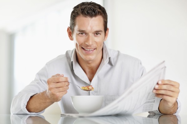 Cheerful mid adult man eating cornflakes and reading newspaper. Photo : Momentimages