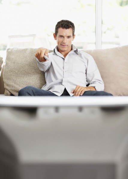 Mid adult man in front of televisionchanging channels. Photo : Momentimages