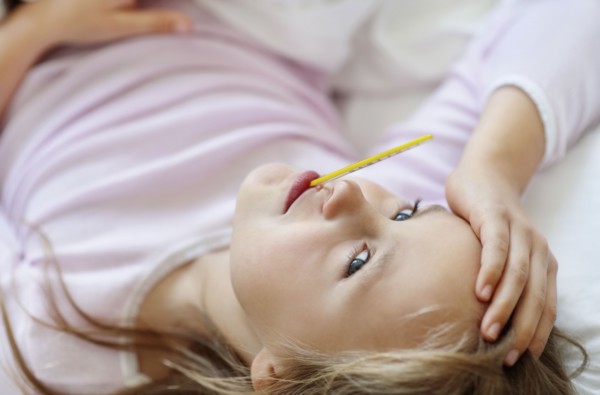 Sad girl (10-11) lying in bed with thermometer in mouth. Photo : Momentimages