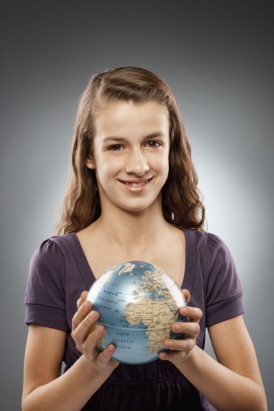 Portrait of girl (12-13) holding globe and looking at camera, studio shot. Photo : FBP