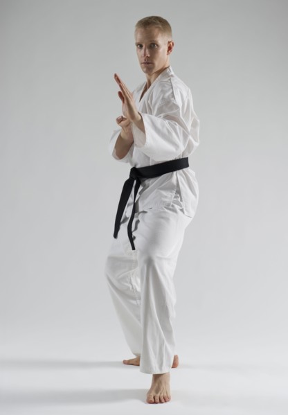 Young man performing karate stance on white background.