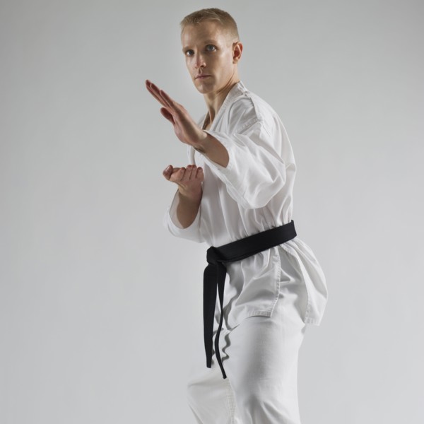 Young man performing karate stance on white background.