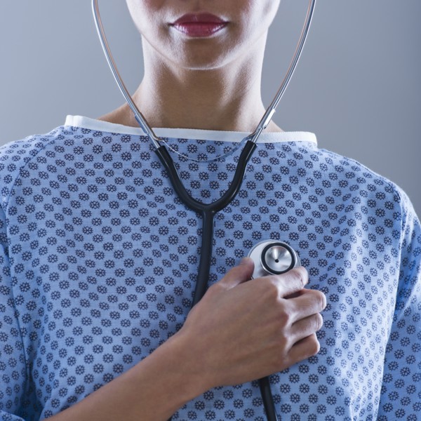 Female patient holding stethoscope to chest.