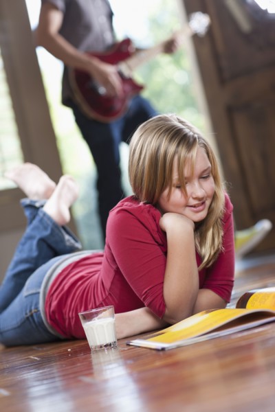USA, Utah, Girl (10-11) reading magazine while man in the background playing guitar. Photo : Tim