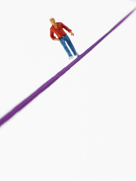Studio shot of male figurine balancing on tightrope. Photo : David Arky