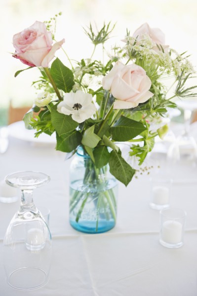 Vase of roses on set dinner table with glasses.
