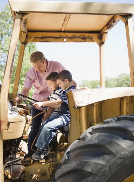 USA, New York, Flanders, Two boys (4-5, 8-9) with father sitting on tractor. Photo : Jamie Grill