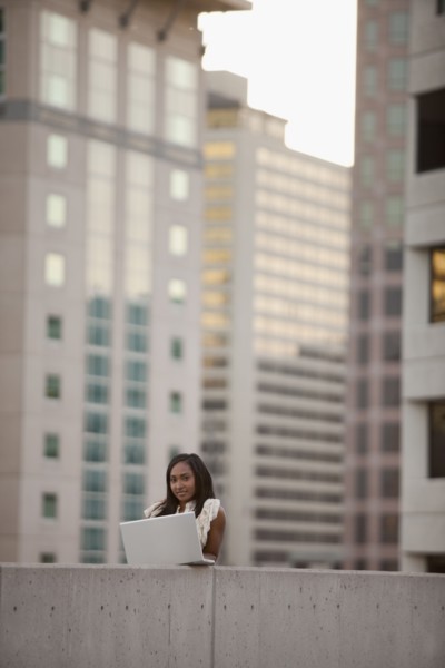 USA, Utah, Salt Lake City, Young businesswoman using laptop in front of skyscrapers. Photo : Mike