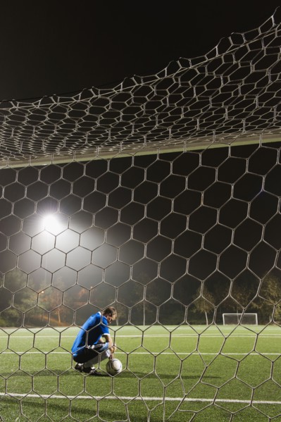 USA, California, Ladera Ranch, goalie on illuminated soccer field at night.