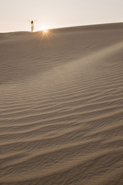 Woman with arms up, standing in desert.