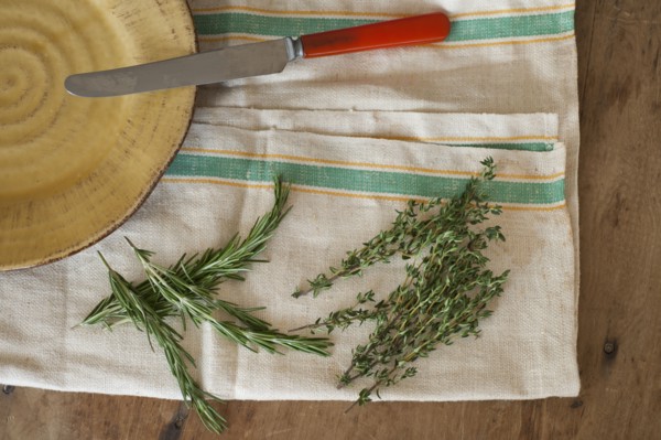 Rosemary and thyme with kitchen knife lying on kitchen cloth, directly above.