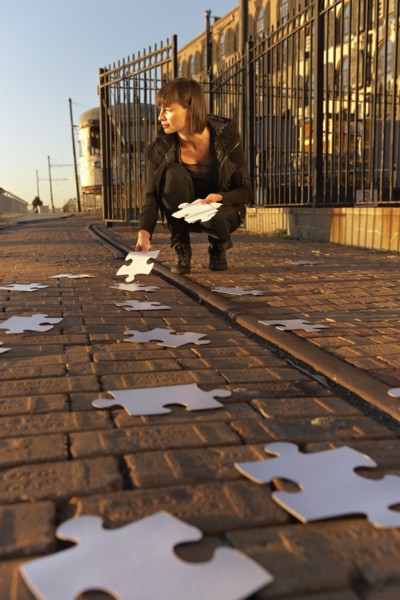 USA, New York City, Brooklyn, woman picking up jigsaw pieces from sidewalk. Photo : Shawn O'Connor
