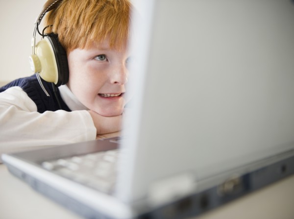 Boy (8-9) wearing headphones, using laptop. Photo : Jamie Grill Photography