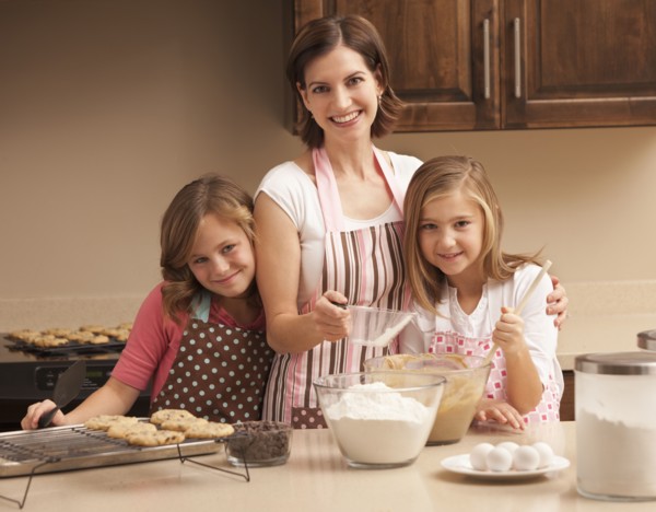 Portrait of mother baking with daughters (10-11) in kitchen. Photo : Mike Kemp