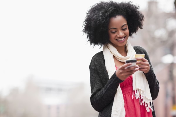 USA, Washington State, Seattle, Cheerful young woman text messaging while holding takeaway coffee.
