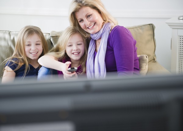 Mother and daughters (8-11) watching tv. Photo : Jamie Grill Photography