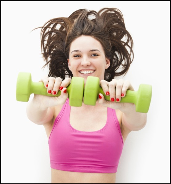 Studio portrait of young woman holding hand weights. Photo : Mike Kemp