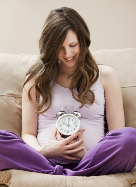 Young pregnant woman holding alarm clock. Photo : Mike Kemp