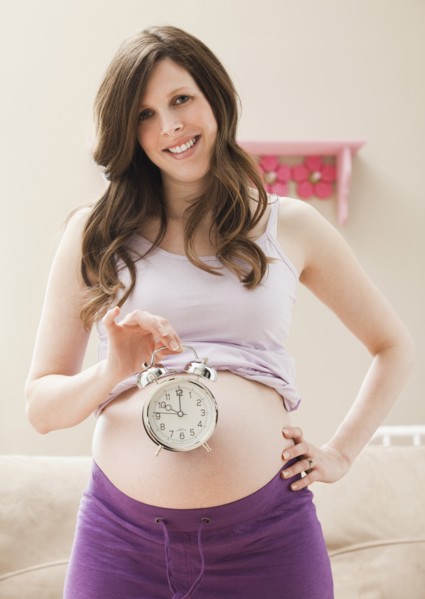 Young pregnant woman holding alarm clock. Photo : Mike Kemp