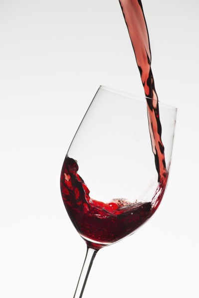 Close up of red wine being poured into glass on white background.