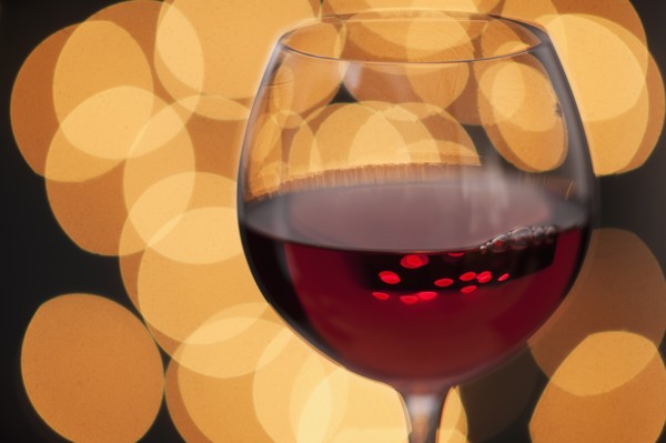 Close up of glass of red wine with defocused lights in background.