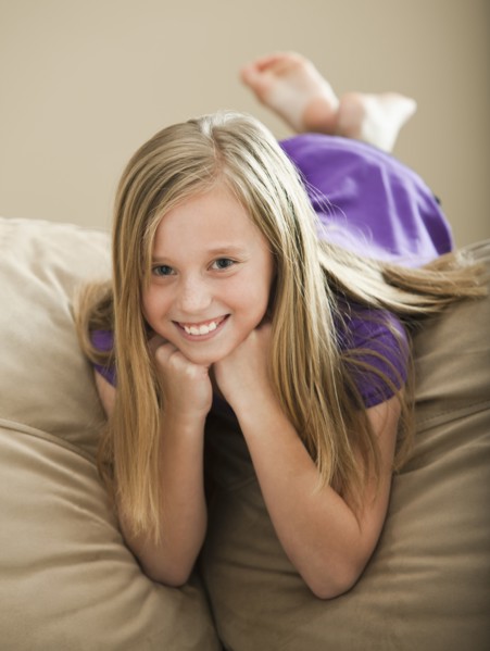 Portrait of girl (8-9) lying on sofa. Photo : Mike Kemp