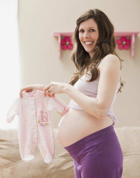Young pregnant woman showing baby clothes. Photo: Mike Kemp