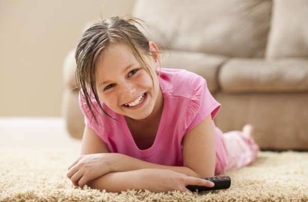 Portrait of girl (10-11) lying on floor holding remote control. Photo : Mike Kemp