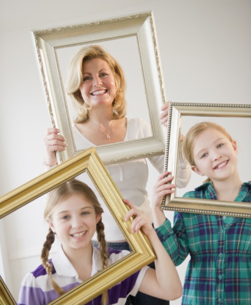 Mother and daughters (8-11) holding picture frames. Photo: Jamie Grill Photography