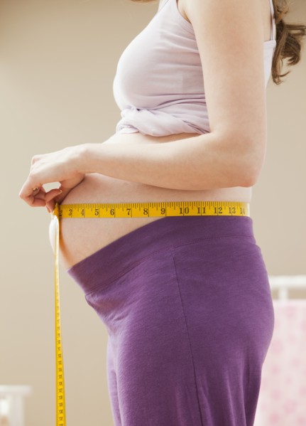 Young pregnant woman measuring belly. Photo : Mike Kemp