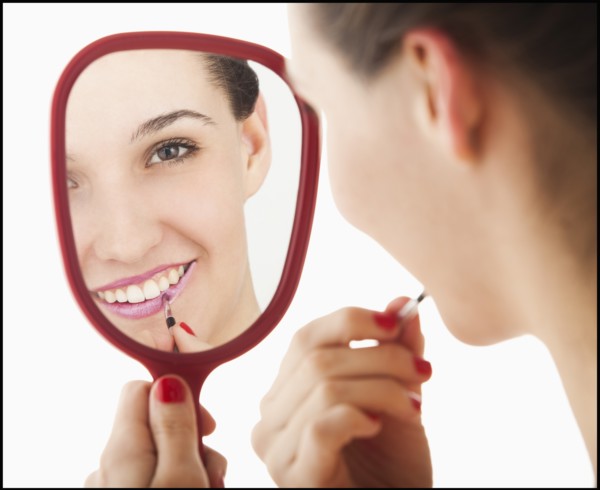 Studio portrait of young woman applying lipstick in mirror. Photo: Mike Kemp