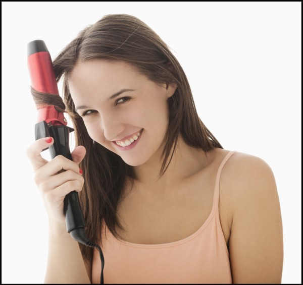 Studio portrait of young woman curling hair. Photo: Mike Kemp