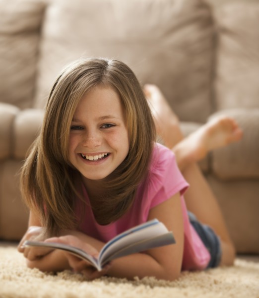Portrait of girl (10-11) lying on rug with book. Photo: Mike Kemp