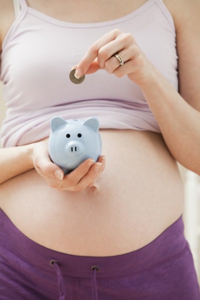 Young pregnant woman putting coin into blue piggybank. Photo : Mike Kemp