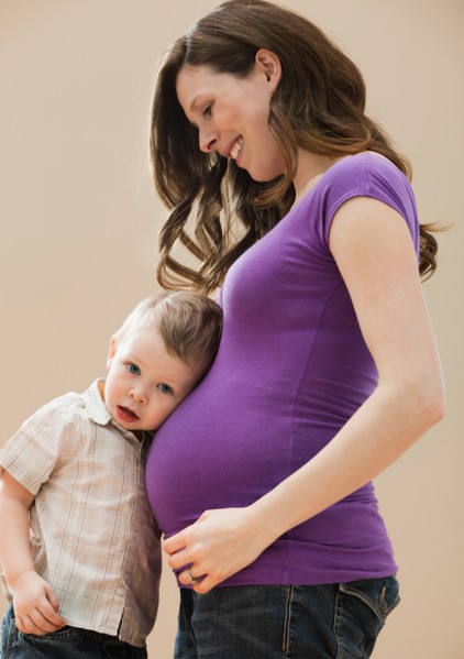 Portrait of boy (2-3) leaning pregnant mother's belly. Photo : Mike Kemp