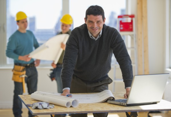 Architect preparing blueprintConstruction workers in background.