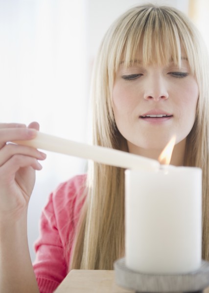 Young woman igniting candle. Photo: Jamie Grill Photography