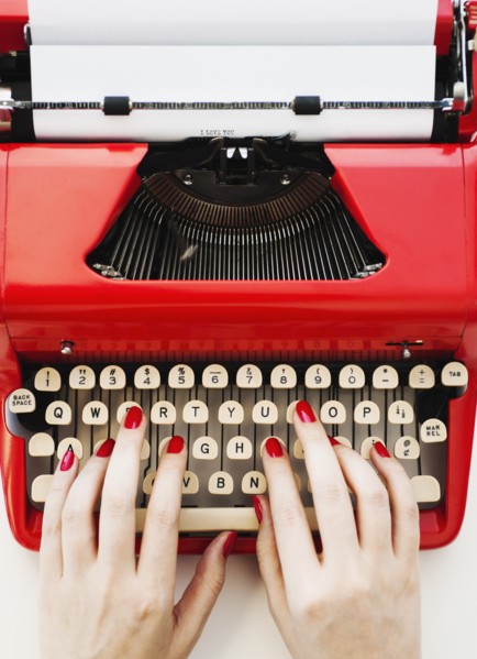 Close up of woman's hands with red nail polish typing on antique typewriter.