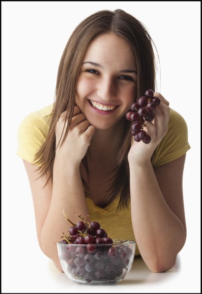 Studio portrait of young woman holding grapes. Photo : Mike Kemp